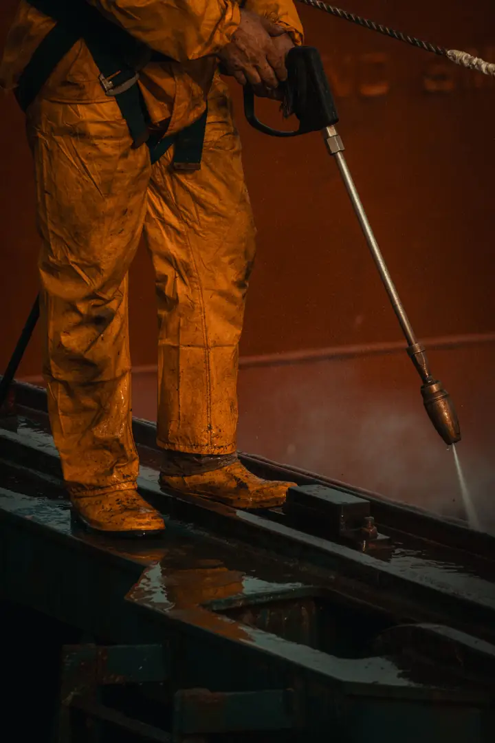 Worker in protective orange coveralls using a high-pressure lance on industrial equipment